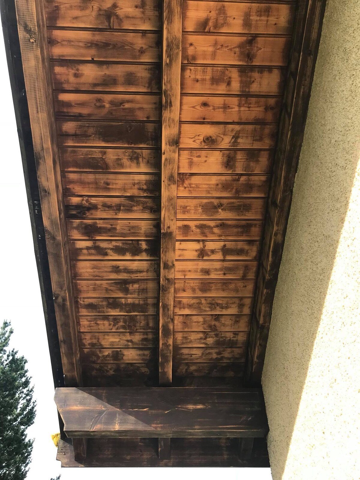 Sous-face d'avant-toit en bois avant travaux, lambris foncé et vernis usé