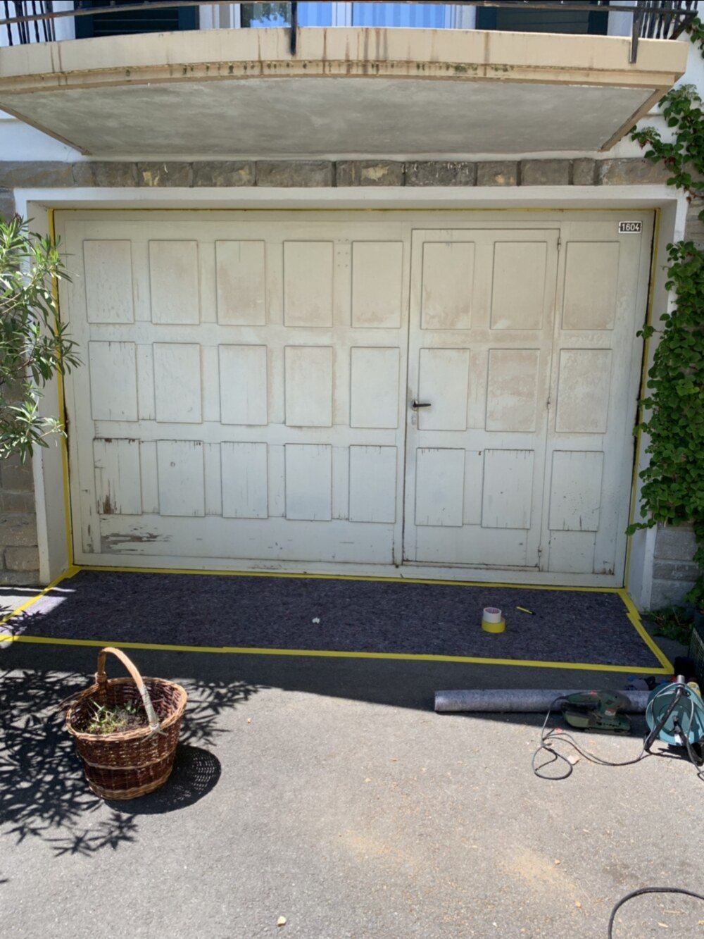 Porte de garage en bois avant travaux, peinture crème écaillée, chantier protégé