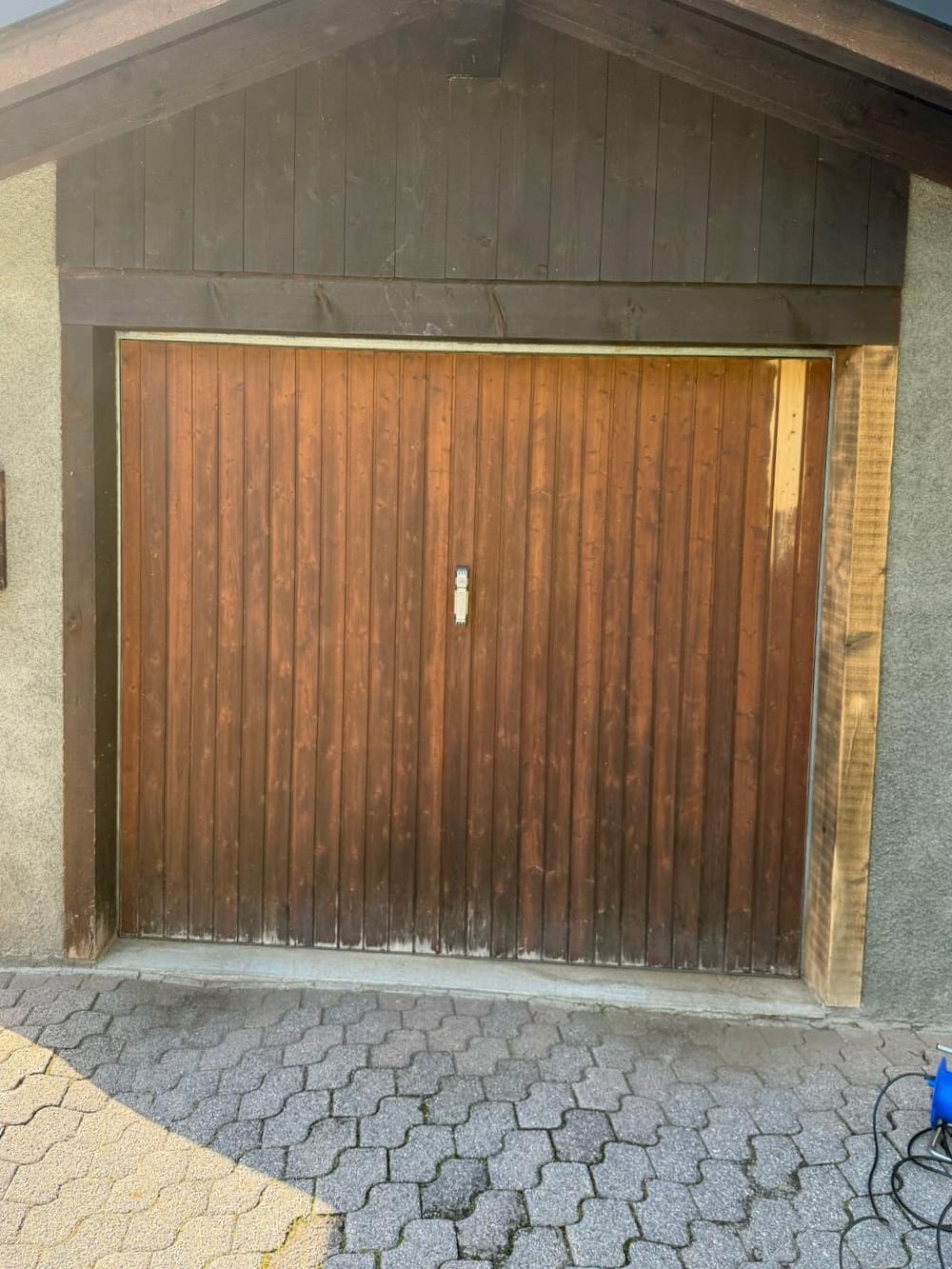 Porte de garage en bois avant travaux, lames délavées et grisées en pied