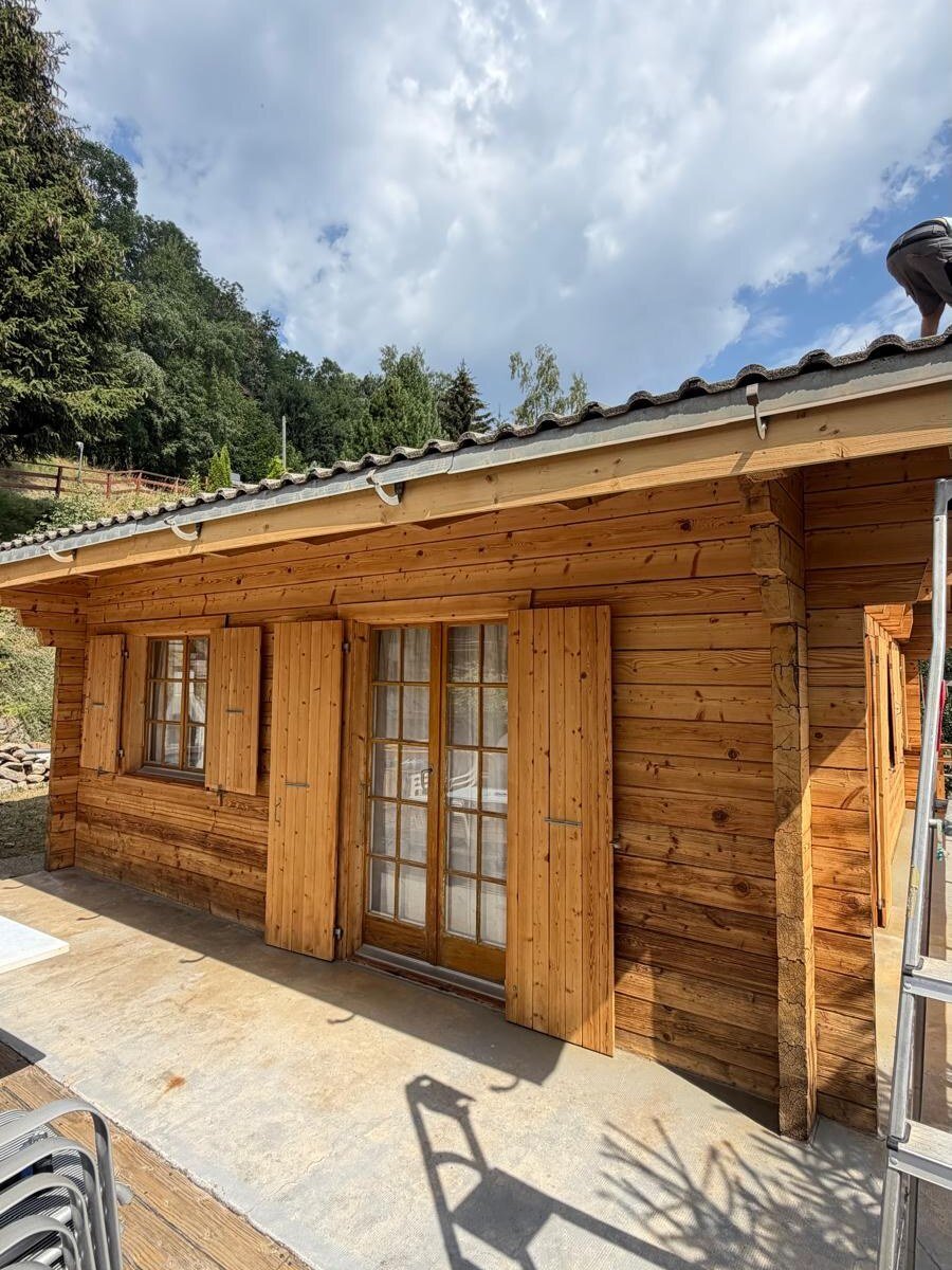 Façade du chalet côté terrasse après sablage, madriers clairs et volets repris
