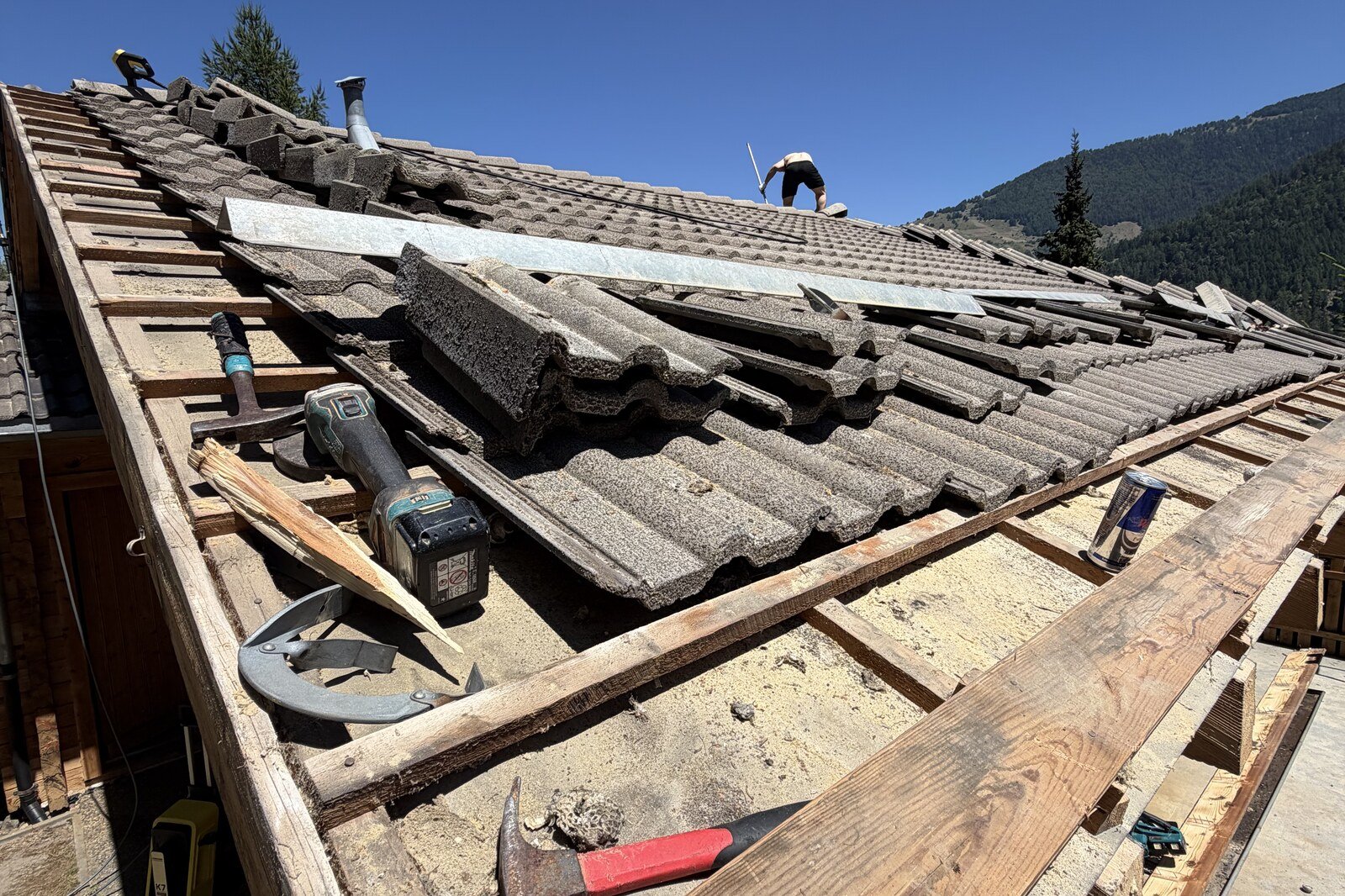 Toiture de chalet en cours de dépose, tuiles enlevées et lattis à nu, montagnes en arrière-plan